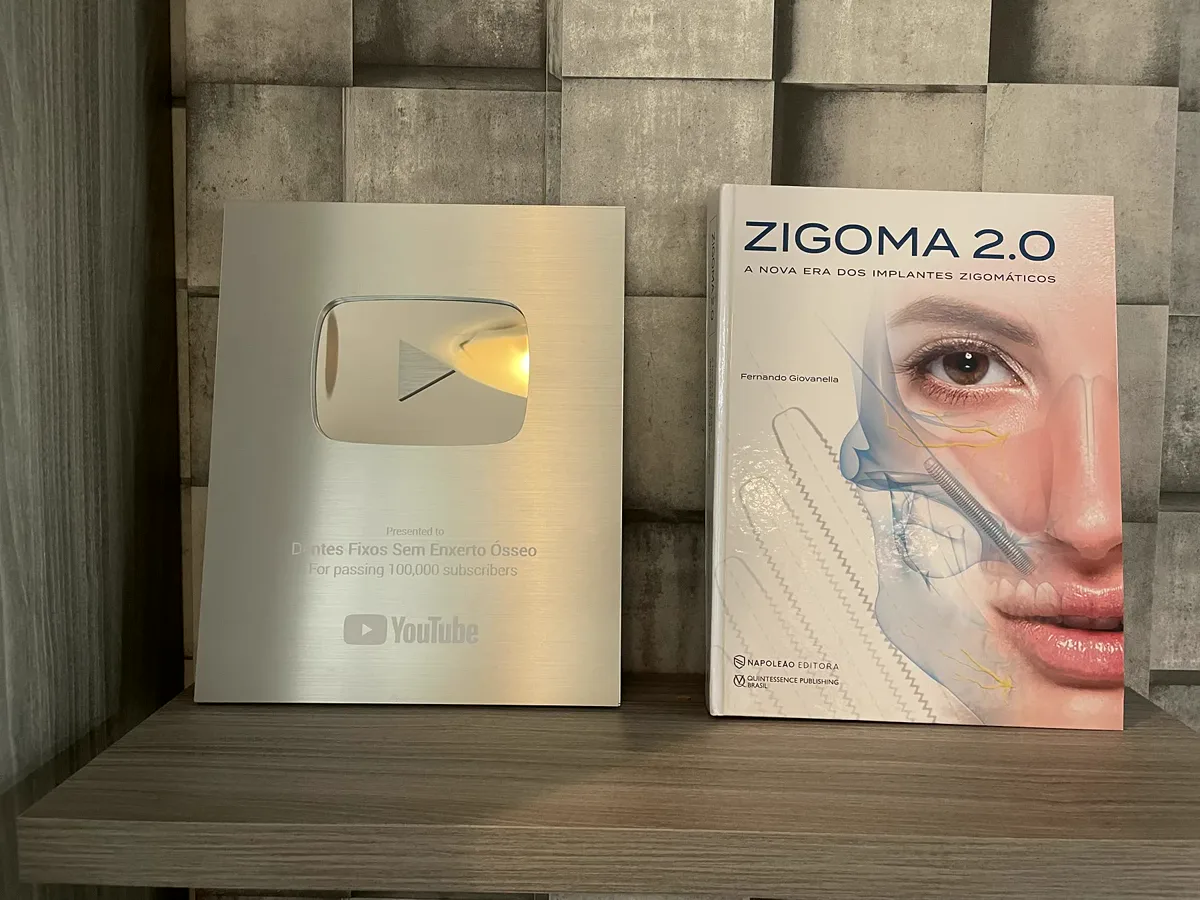 O livro ZIGOMA 2.0 ao lado da placa do YouTube de 100 mil inscritos